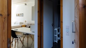 A hallway leading to a dining area with a table and chairs, a white wall with a shelf, and a door. - Eupnea | Studio Apartment, Art by PraXis Apartments (Limassol)