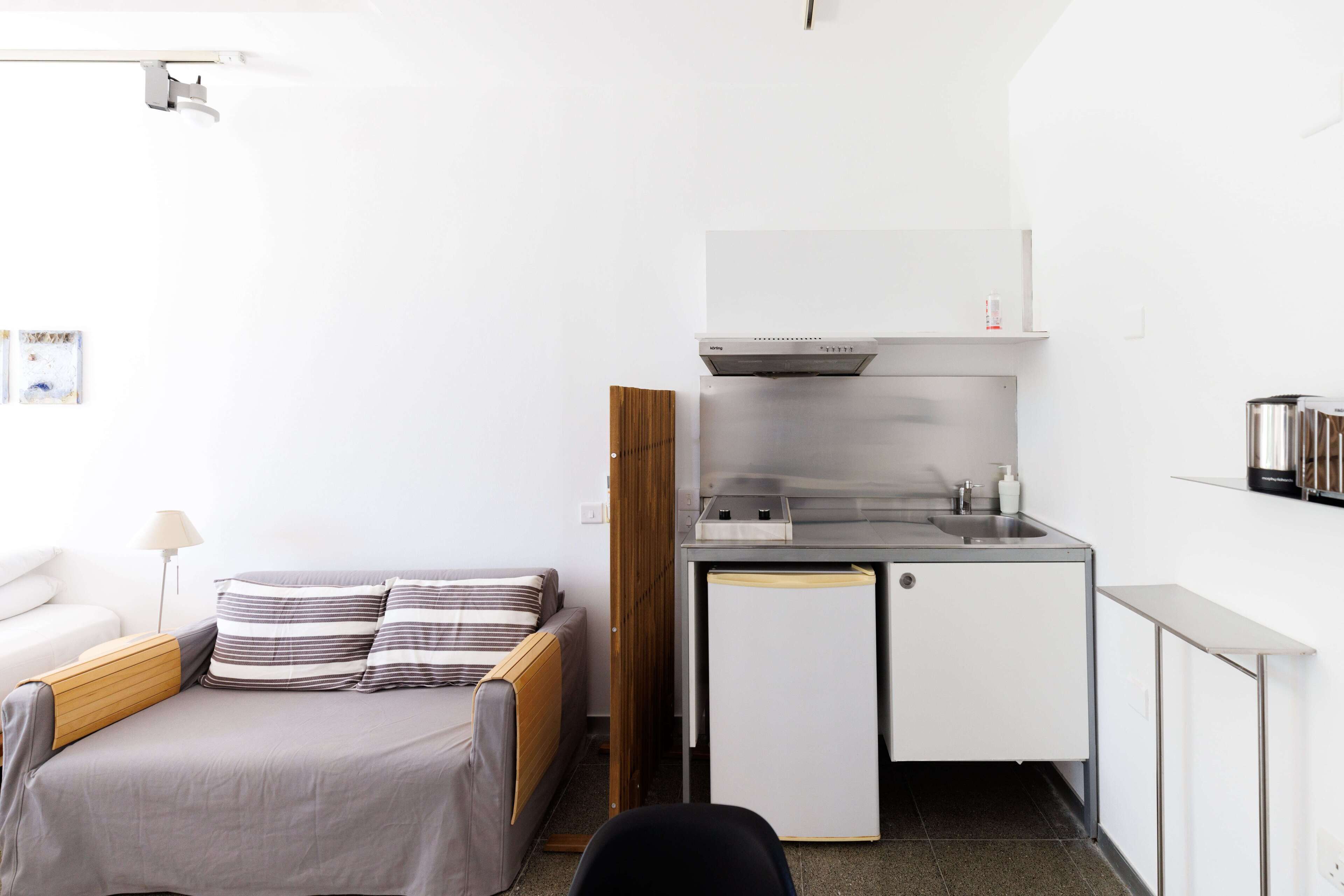 Una habitación compacta con cama, una kitchenette pequeña y un escritorio.