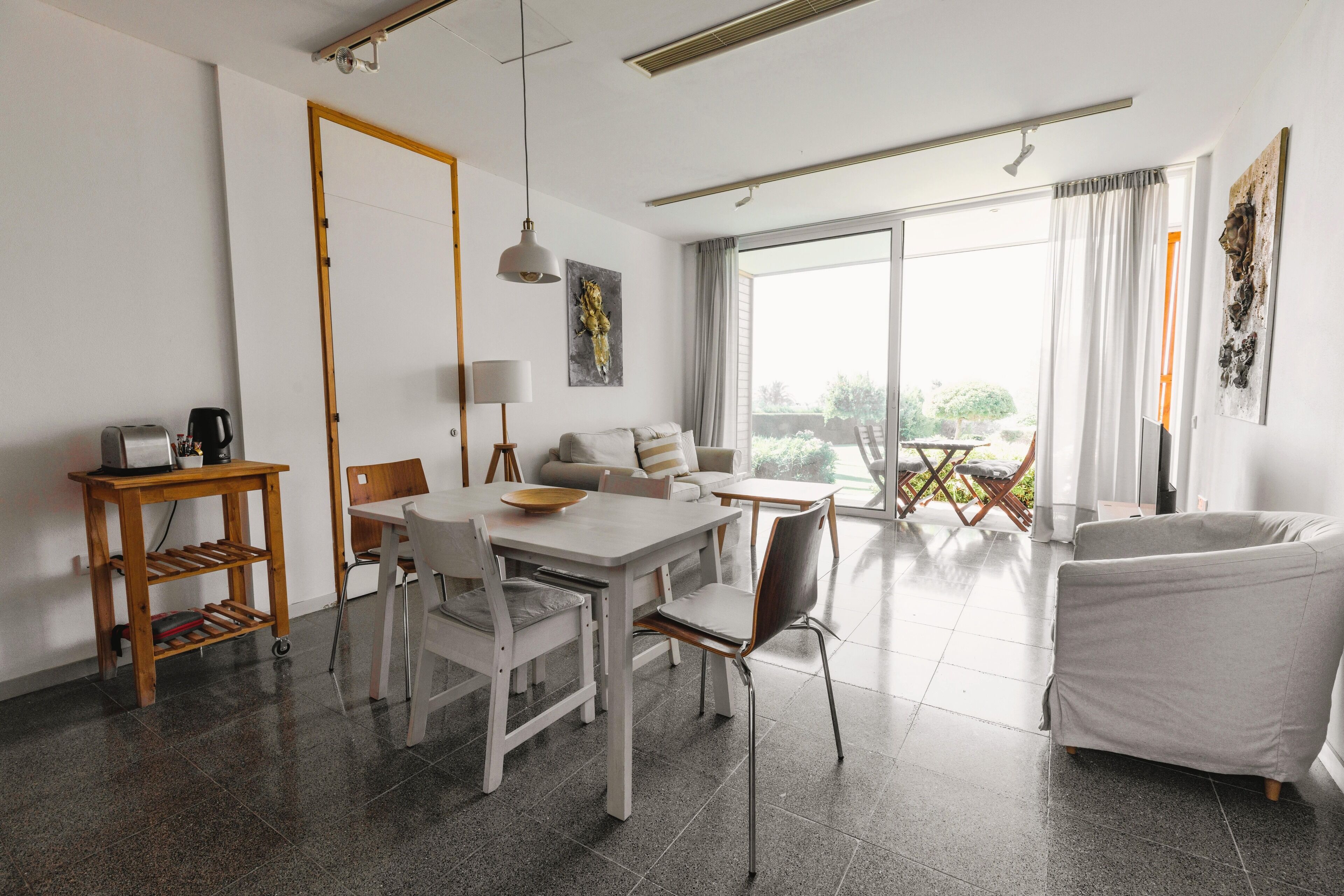 Een moderne woonkamer met een eethoek, een bank, een salontafel en uitzicht op het groen door grote ramen.