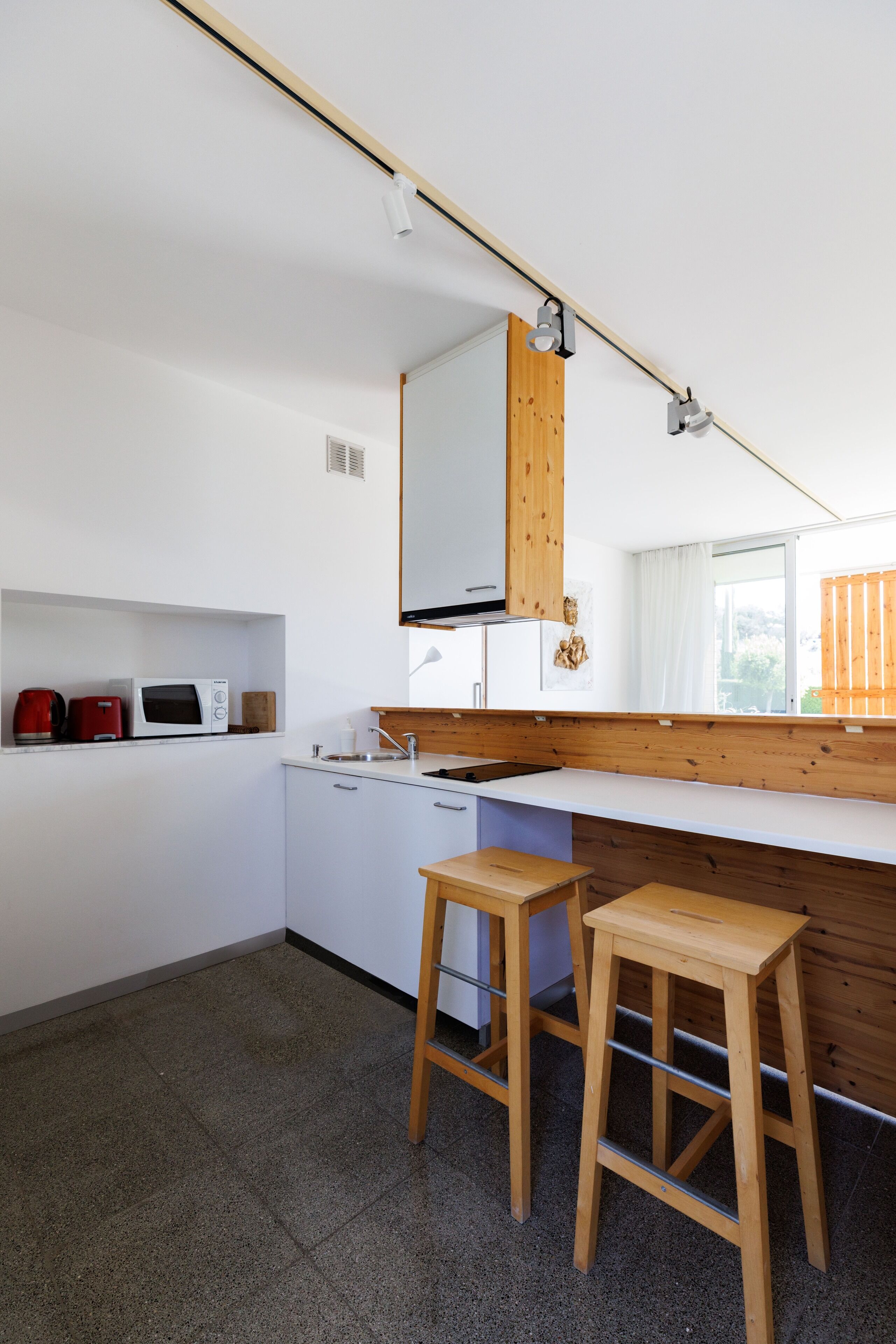 Una cocina moderna con armarios blancos, encimera de madera, un lavamanos y un taburete de madera.