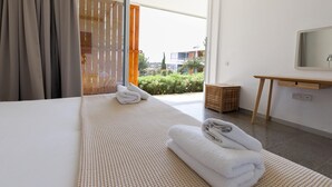 A hotel room with a large bed, a wooden bedside table, a small wooden stool, and a view of greenery and buildings outside. - Euphonia | One-Bedroom Apartment, Art by PraXis Apartments (Limassol)