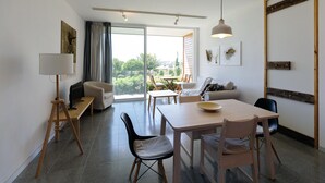 A modern living room with a dining area, large windows, and a view of greenery outside. - Euphonia | One-Bedroom Apartment, Art by PraXis Apartments (Limassol)