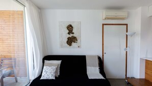 A modern room with a black sofa, a wooden table, a white air conditioning unit, and a wooden door.