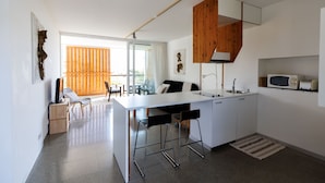 A modern kitchen with a white countertop, bar stools, a wooden ceiling, and a view to the outside.