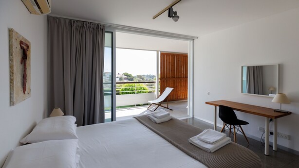 A hotel room with a large bed, a desk, a chair, a window with a view, and a balcony.
