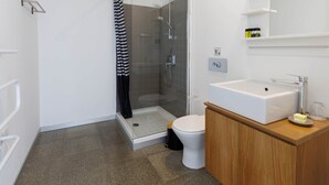 Une salle de bain moderne avec une douche à parois de verre, des toilettes blanches et un meuble-lavabo en bois doté d’un miroir.