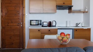Une cuisine compacte avec des meubles en bois, un four à micro-ondes, un grille-pain, une bouilloire et un saladier rempli de fruits sur la table.