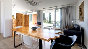 Ein modernes Wohnzimmer mit einem Holzessttisch, weißen und schwarzen Stühlen, einem schwarzen Sofa und einem großen Fenster mit Vorhängen.