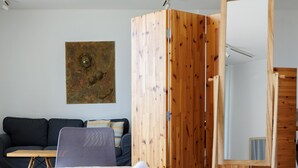Ein ordentlich gemachtes Bett mit gefalteten Handtüchern, ein Holzschrank, ein kleiner Tisch und eine Couch in einem modernen Zimmer mit schlichtem Design.