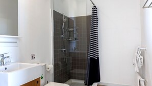 Ein modernes Badezimmer mit einem Holzwaschtisch, einer weißen Toilette, einer Duschkabine aus Glas und einem gestreiften Handtuch, das an der Duschkabinentür hängt.