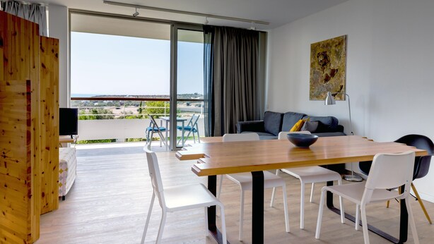 Ein modernes Wohnzimmer mit einem Holzesstisch, weißen Stühlen, einer Couch und einem Balkon mit Blick.