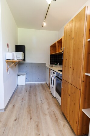 Une cuisine de taille réduite, dotée de meubles en bois, d’un lave-linge et d’un four à micro-ondes.