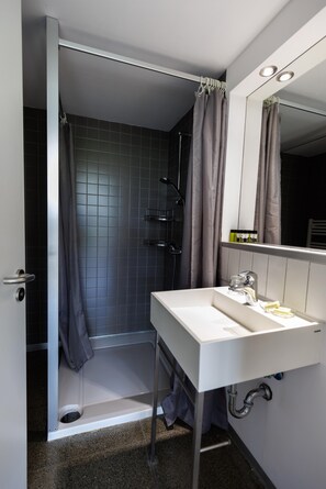 Une salle de bain moderne avec un lavabo blanc, une douche avec un rideau et un miroir au-dessus du lavabo.
