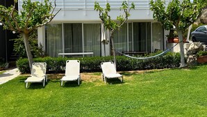 Een modern gebouw met grote ramen, een gazon en drie witte lounge fauteuils.