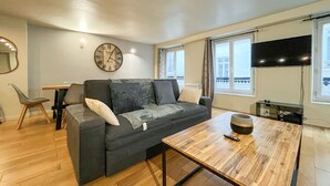 Ein modernes Wohnzimmer mit grauem Sofa, Couchtisch aus Holz und einer Wanduhr.