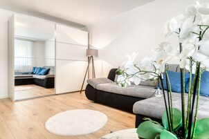 Een moderne woonkamer met een bank, een rond vloerkleed, een vloerlamp en witte orchideeën.