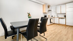 A modern kitchen with white cabinets, a dining table with black chairs, and a wooden floor. - Gartenferienwohnung Arlberg (Bludenz)