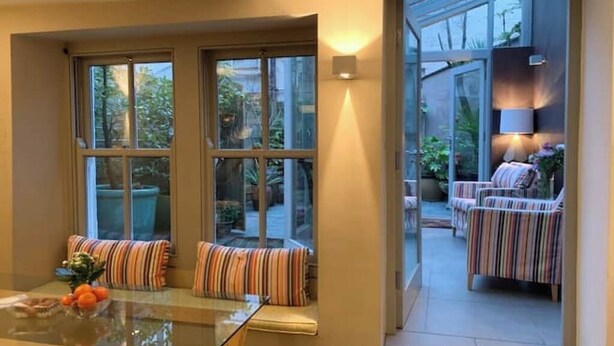 A conservatory with a glass door leading to an outdoor seating area with striped cushions and a table with fruit.