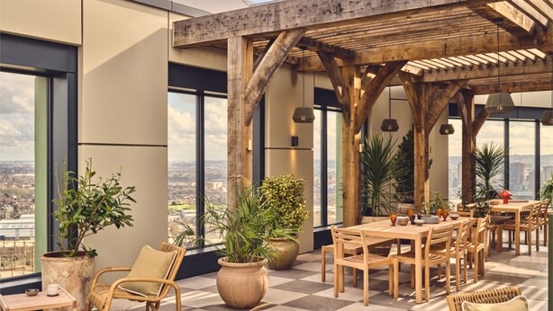 Een terras op het dak met een geruite vloer, een houten pergola en een eethoek met tafels en stoelen.
