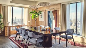Een moderne eethoek met een grote tafel, zes stoelen, een potplant en uitzicht op de stad door grote ramen.