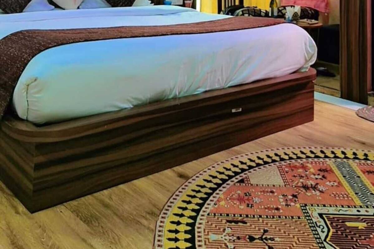 A bedroom with a large bed, a ceiling light, a wall-mounted TV, and a patterned rug.