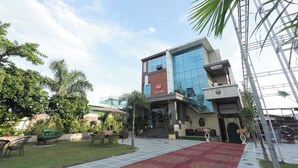 Ένα σύγχρονο ξενοδοχείο με γυάλινη πρόσοψη, μια κόκκινη επιγραφή με το λογότυπο «SRG Inn» και ένα κόκκινο χαλί που οδηγεί στην είσοδο.