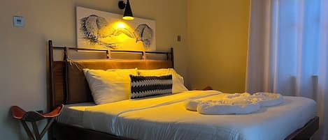 A neatly made bed with white linens, a black and white patterned pillow, and two white towels.