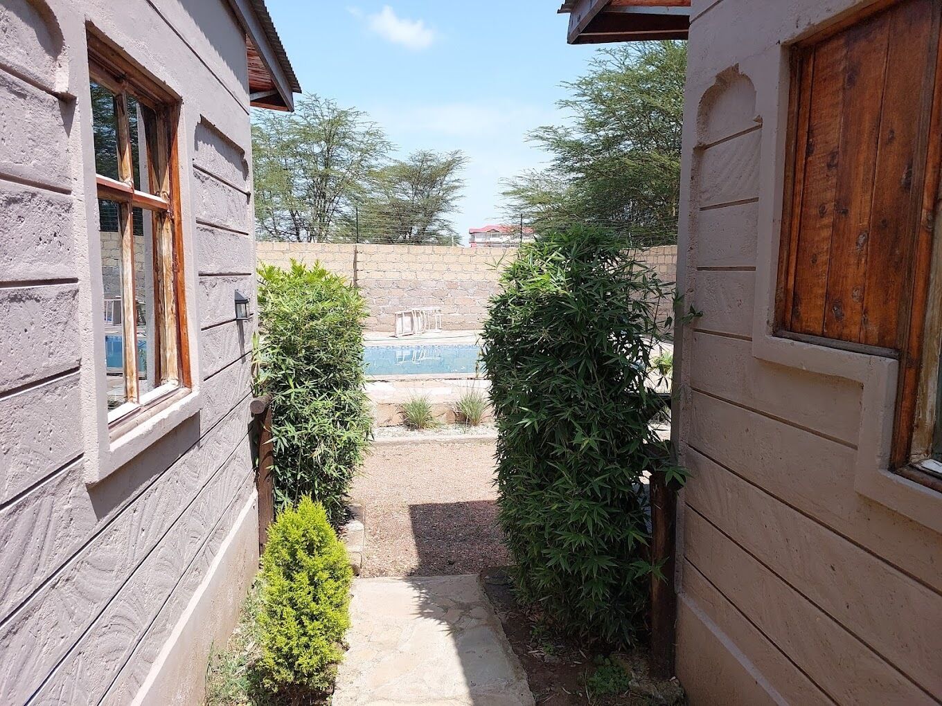 A narrow pathway leading to a pool area with a stone pathway and wooden fencing.