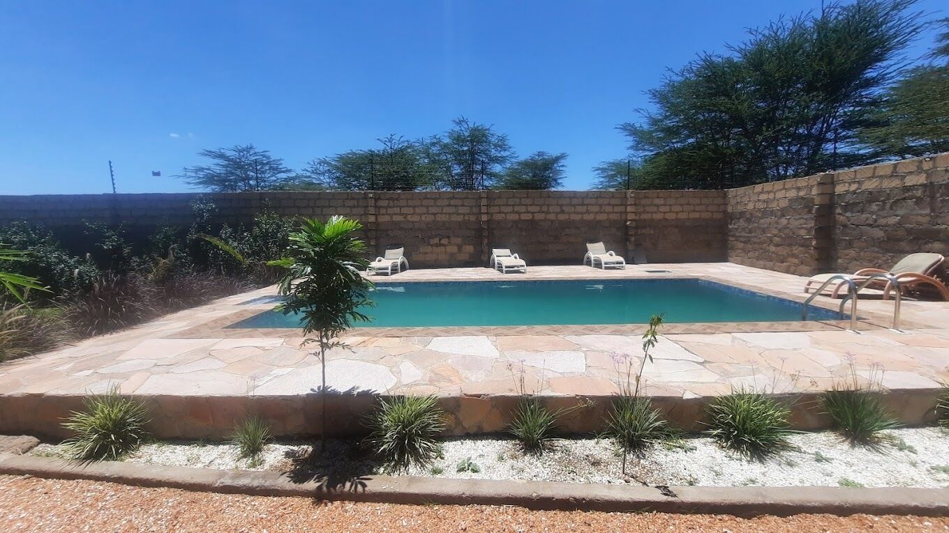 A swimming pool with lounge chairs, surrounded by a stone wall and various plants.