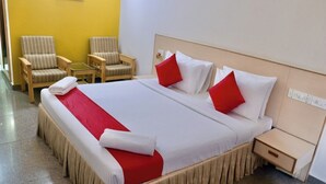 A hotel room with a large bed, two armchairs, a nightstand, and a yellow wall. - Sweet Crystal Homes (Bengaluru)
