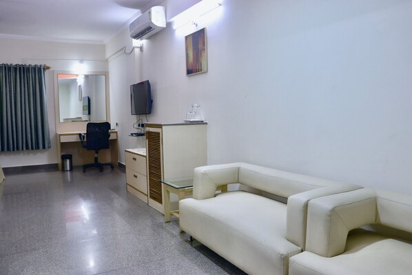 A hotel room with a sofa, a desk with a computer, a chair, a TV, and a bedside table. - Sweet Crystal Homes (Bengaluru)