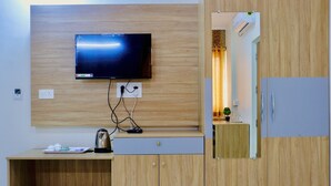 A modern room with a flat-screen TV mounted on a wooden wall, a small wooden table with a kettle, and a wardrobe with a mirror. - Sweet Crystal Homes (Bengaluru)