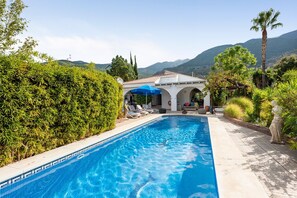 A swimming pool with lounge chairs, a pergola with a blue umbrella, and a statue.