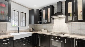 A modern kitchen with dark cabinetry, a double sink, a built-in oven, and a stainless steel range hood. - Holiday Home 'Villa Eden' with Mountain View, Wi-Fi and Air Conditioning (Alcaucín)