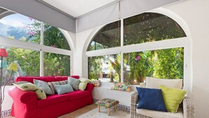 A conservatory with a red sofa, wicker furniture, and a view of lush greenery. - Holiday Home 'Villa Eden' with Mountain View, Wi-Fi and Air Conditioning (Alcaucín)