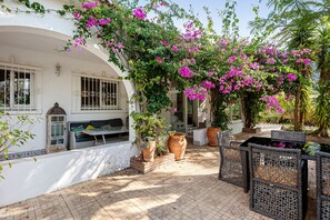 A patio with potted plants, wicker furniture, and a white building with arched windows. - Holiday Home 'Villa Eden' with Mountain View, Wi-Fi and Air Conditioning (Alcaucín)
