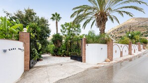 A gated entrance with a sign reading 'CASA,' surrounded by palm trees and a hilly landscape. - Holiday Home 'Villa Eden' with Mountain View, Wi-Fi and Air Conditioning (Alcaucín)