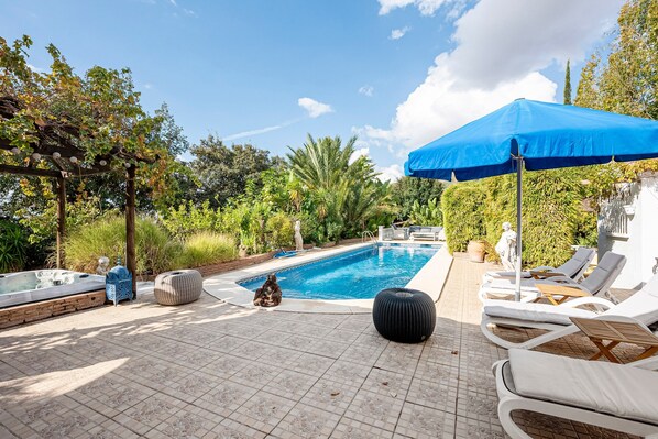 A poolside area with lounge chairs, a hot tub, and a pergola.