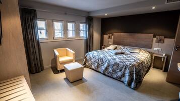Une chambre d’hôtel moderne avec un grand lit, une chaise, une petite table et une fenêtre avec des rideaux.