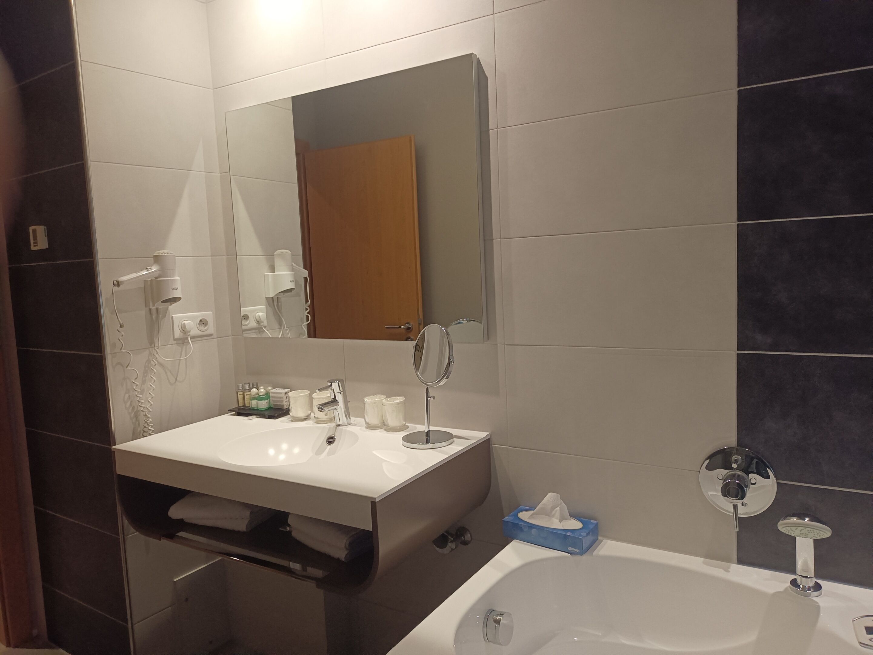 A modern bathroom with a white sink, a mirror, a hairdryer, and a bathtub.