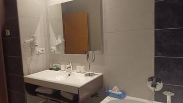 A modern bathroom with a white sink, a mirror, a hairdryer, and a bathtub.