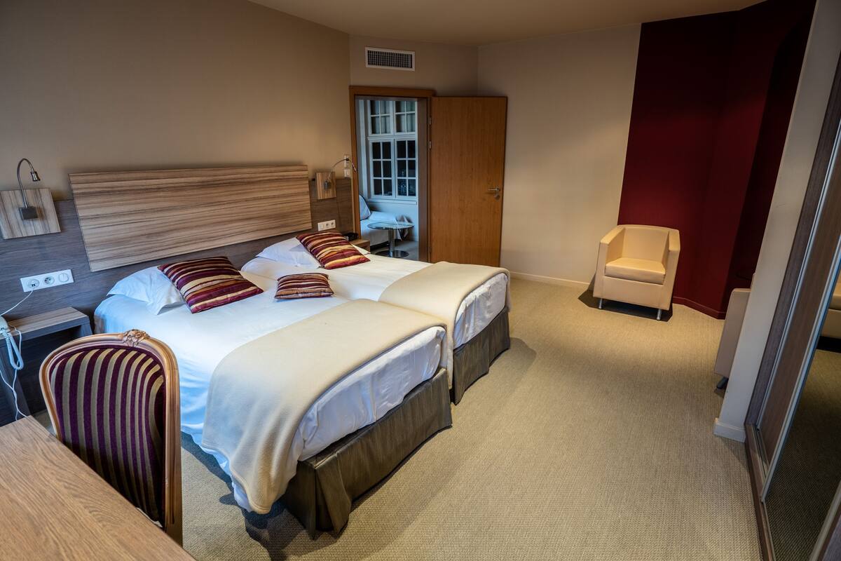 A hotel room with two beds, a desk, a chair, a wardrobe, and a window.