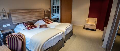 A hotel room with two beds, a desk, a chair, a wardrobe, and a window.