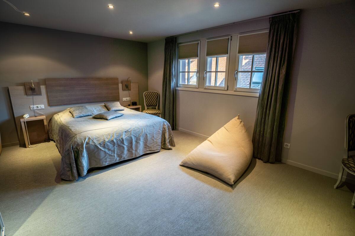A modern bedroom with a large bed, a chair, and a window with curtains.
