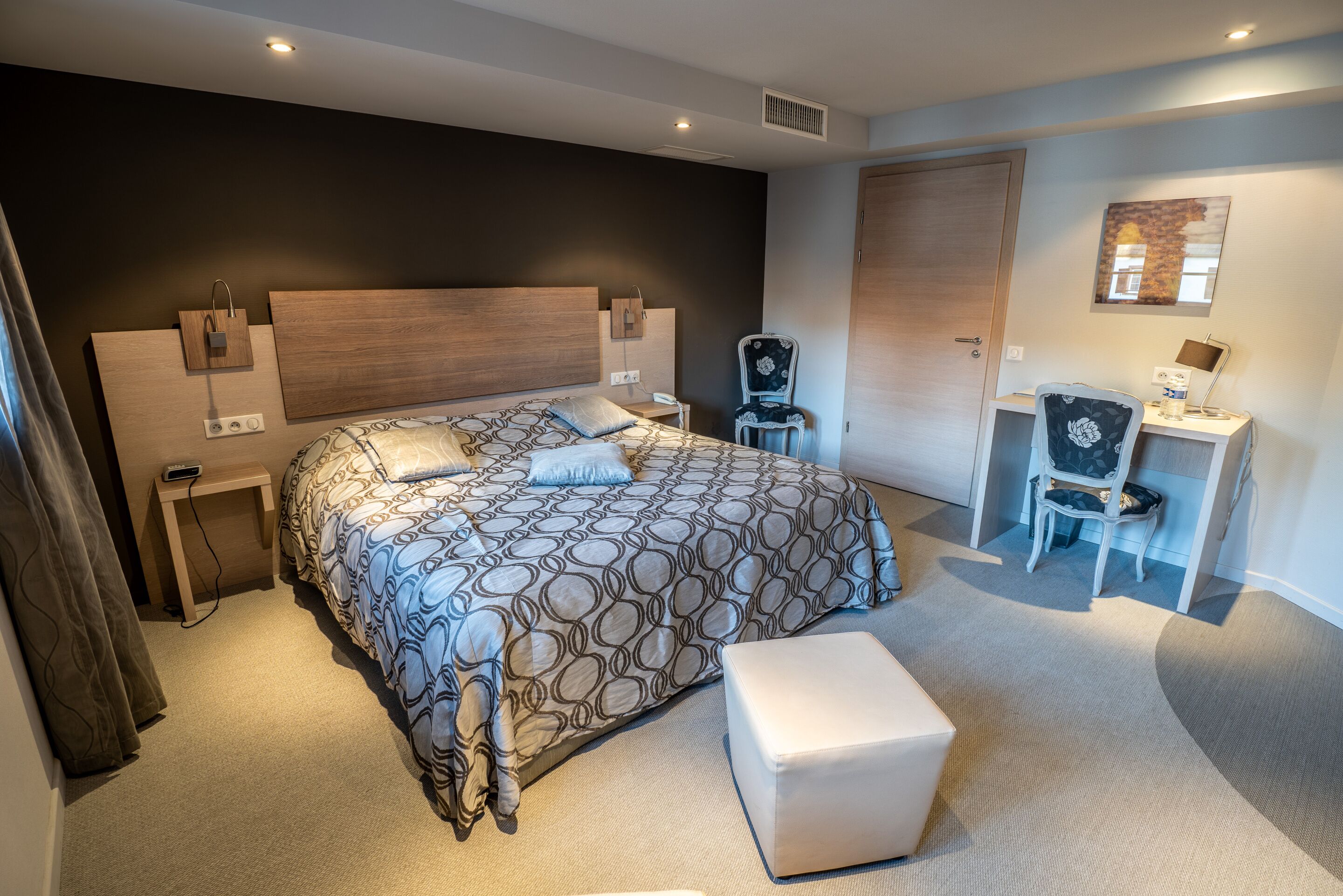 A modern hotel room with a large bed, a desk, a chair, and a small table.