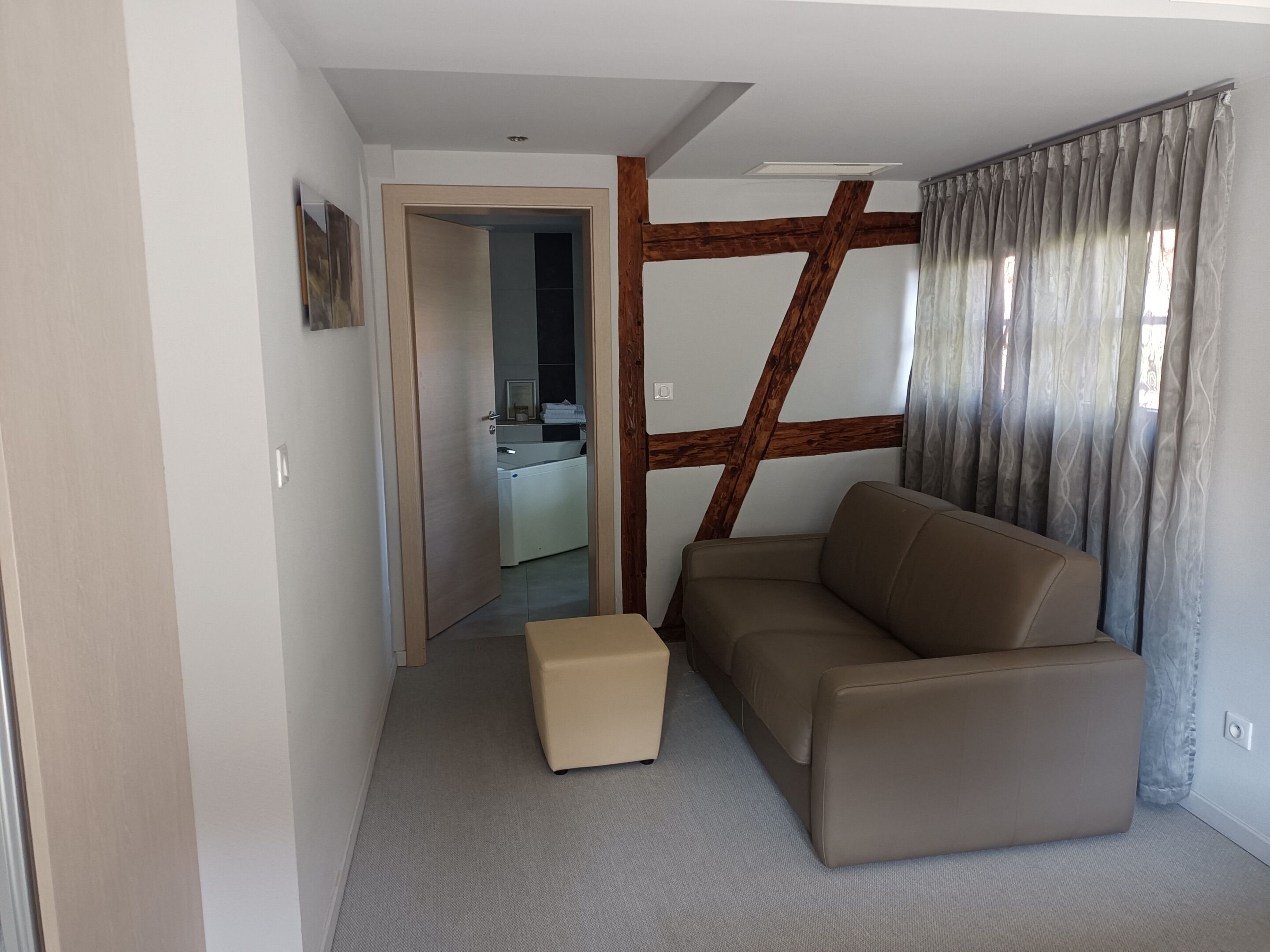 Una sala moderna con un sofá, un reposapiés pequeño y una estructura de vigas de madera.