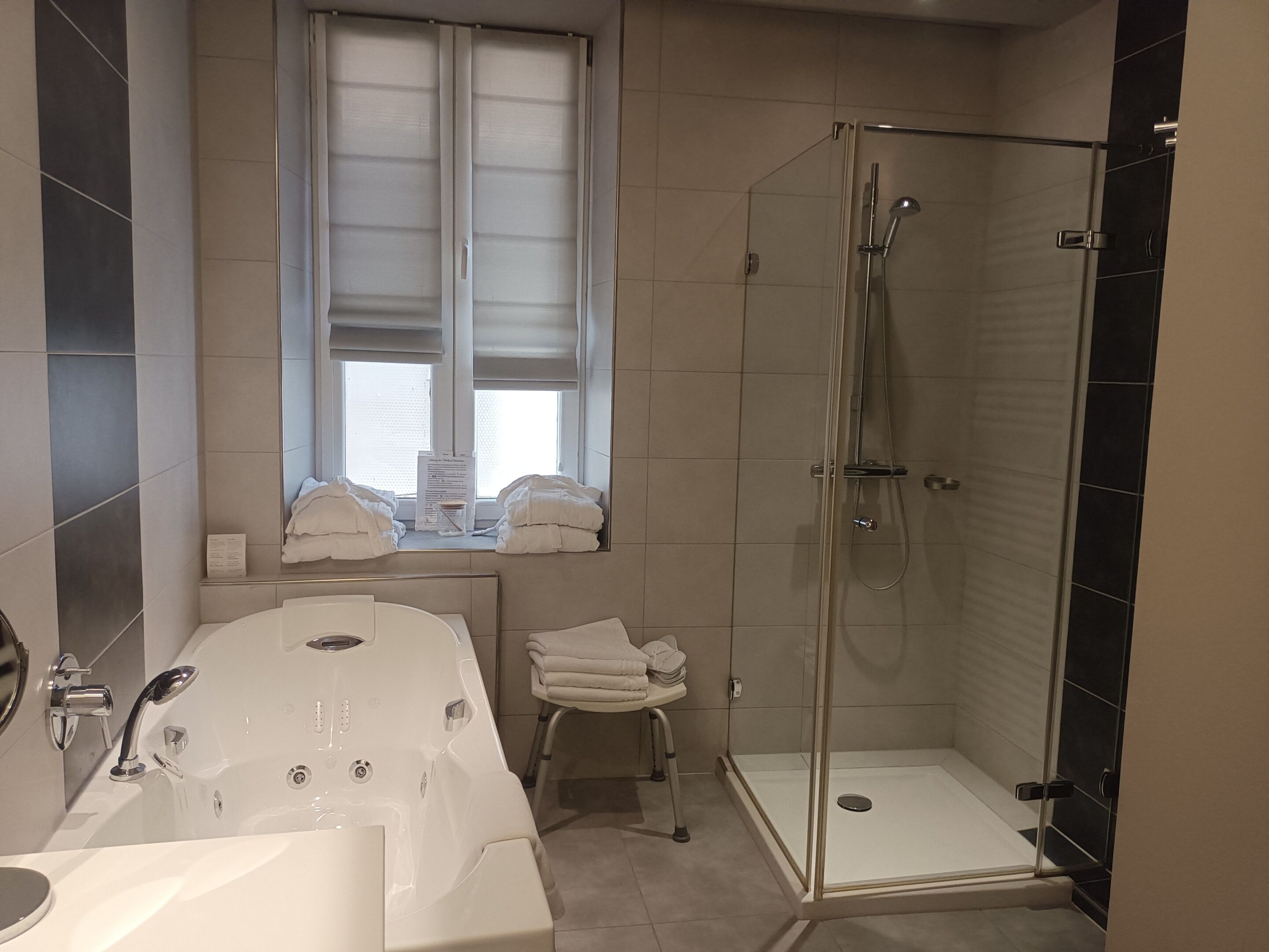 A modern bathroom with a bathtub, a shower, and a window.