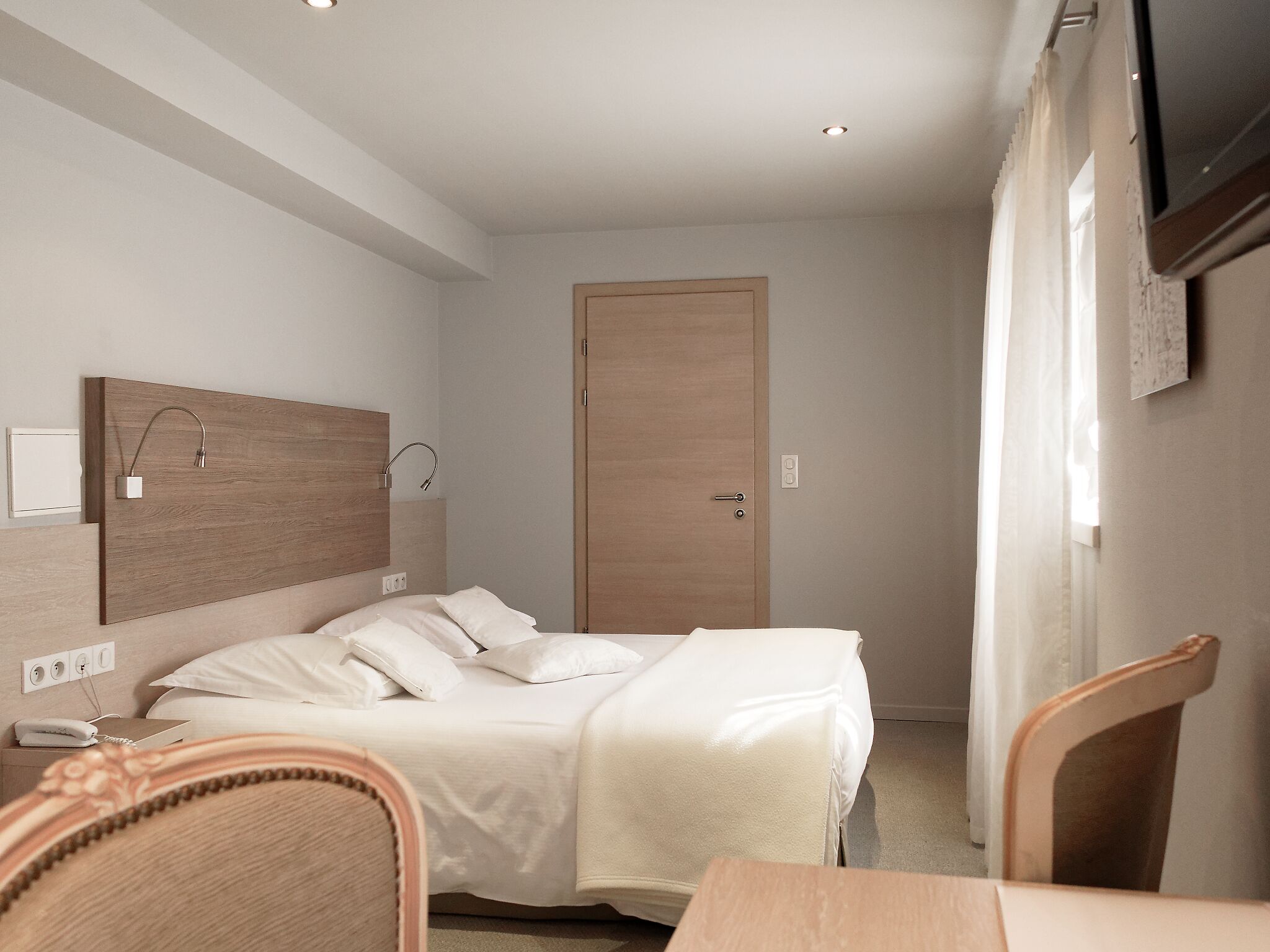 A small, modern bedroom with a bed, bedside table, and a TV mounted on the wall.