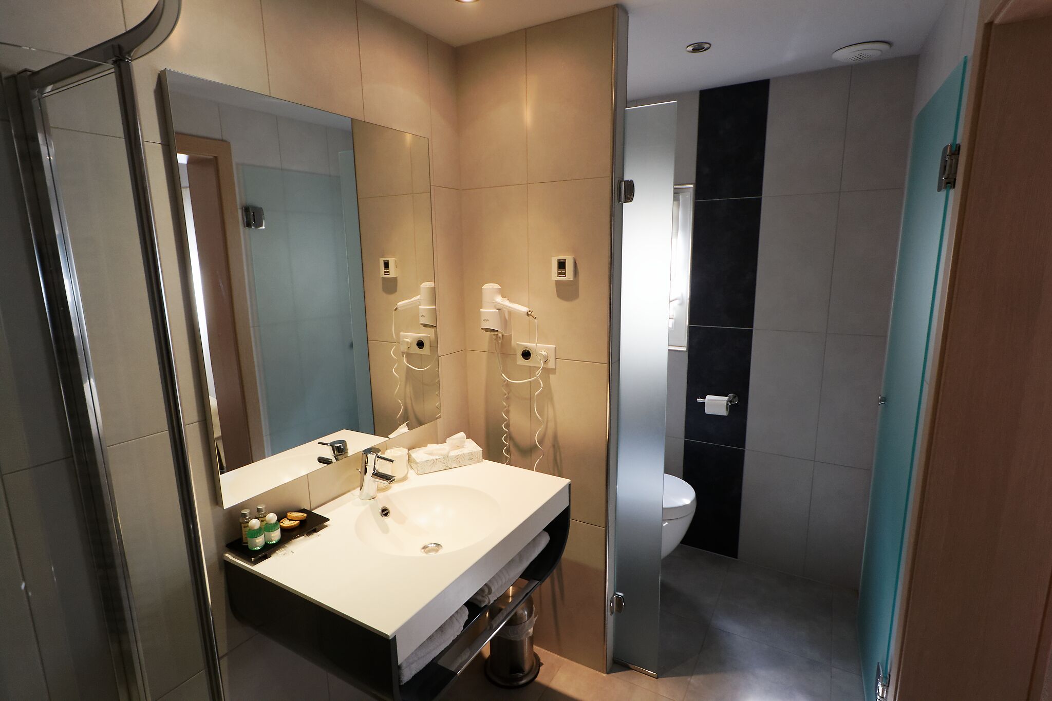 A modern bathroom with a large mirror, a sink, and a toilet.
