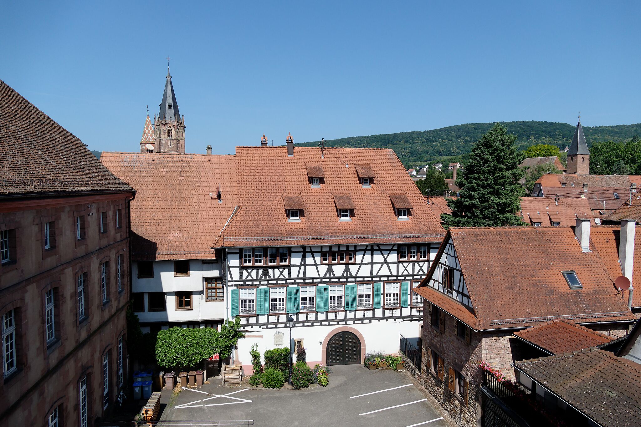 Ein traditionelles Fachwerkhäus mit Innenhof, einem Kirchturm im Hintergrund und einer hügeligen Landschaft.